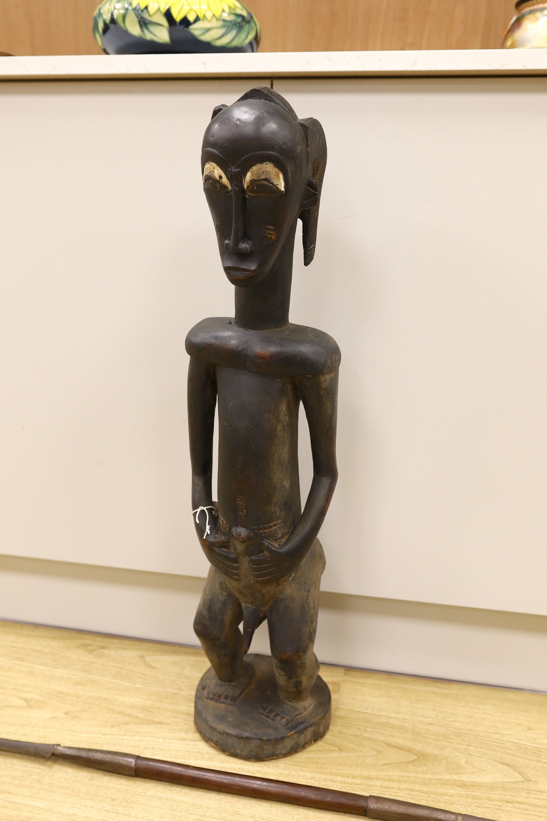 An African Baoule crouched tribal figure, together with a spear, 156cm long